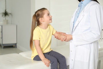 Professional orthopedist examining little patient's arm in clinic