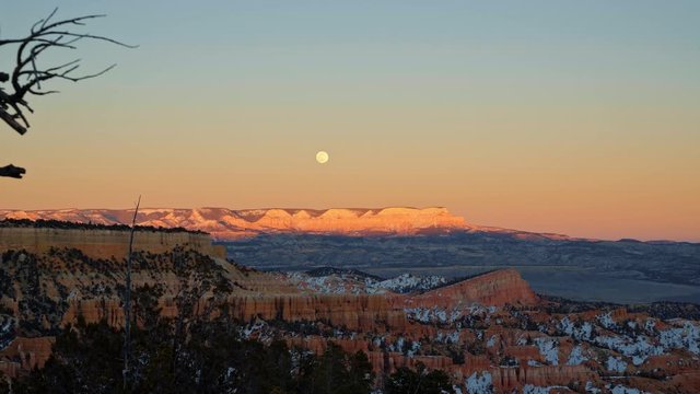 Stunning winter sunset looking out to the famous natural amphitheater in Bryce Canyon National Park, Utah. During the super moon which is rising and illuminating the rocks.