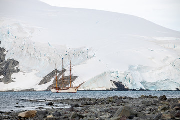 sailing Expedition ship in antarctica surrounded by ice in front of a glacier and rocks 