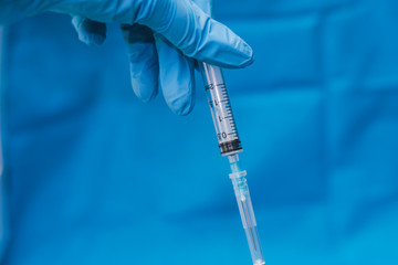 Hands in blue gloves with hepatitis vaccine in a transparent bottle. Treatment of COVID 19 or...