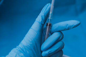 Hands in blue gloves with hepatitis vaccine in a transparent bottle. Treatment of COVID 19 or...