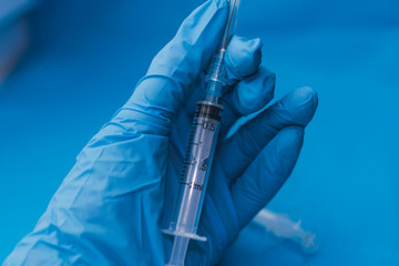 Hands in blue gloves with hepatitis vaccine in a transparent bottle. Treatment of COVID 19 or...