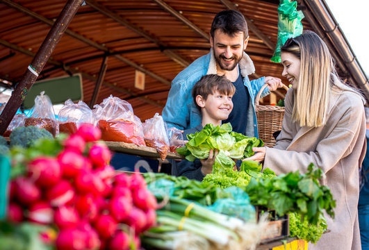 Family Buying Fresh Vegetables At Farmers Market Stall