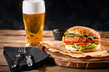 Delicious hot spicy black burger with chili pepper and glass of beer on cutting board on white wood...
