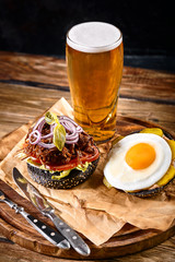 Delicious hot spicy black burger with chili pepper and glass of beer on cutting board on white wood table