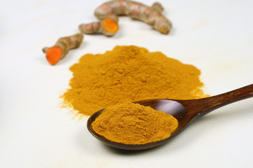 Turmeric powder in a wooden spoon and fresh turmeric roots isolated on a white background is an ingredient in turmeric foods and ingredients in skin care products. Turmeric helps strengthen the skin.
