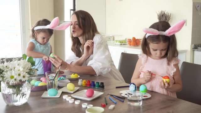 happy family preparing for easter. mother with daughters with funny bunny ears painting easter eggs together