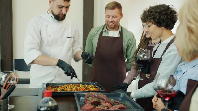 Diverse group of trainees men and women are learing food preparation watching professional chef smiling in cookery school. People and meals concept.