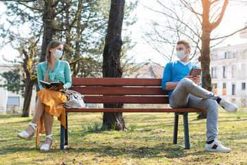 Woman and man in social distancing sitting on bench - obrazy, fototapety, plakaty