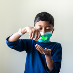 Sick Muslim Kid with surgical mask squeezing hand sanitizer onto his hand. Precaution during Covid-19 Coronavirus scare. Shallow depth of field