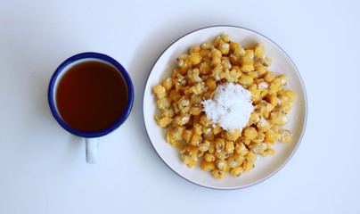 Grontol jagung and a cup of tea on white background.  Grontol jagung is traditional snacks in Indonesia. Boiled shelled corn sprinkled with grated coconut.