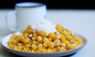 Grontol jagung and a cup of tea on white background.  Grontol jagung is traditional snacks in Indonesia. Boiled shelled corn sprinkled with grated coconut.