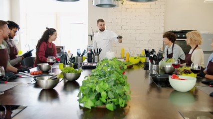 Cooking teacher handsome man in uniform is talking to diverse group of people students in kitchen teaching cookery. Hobby, occupation and food concept.