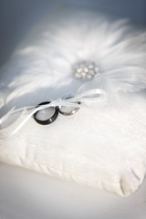 Wedding bands tied to a white pillow made with feathers and pearls