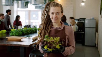 Portrait of attractive young lady with dreadlocks smiling standing in cooking school holding salad bowl enjoying cookery education. People and lifestyle concept.
