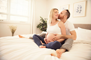 Beautiful pregnant woman and her handsome husband spending time together in bed