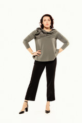 Fototapeta premium A serious woman in a gray blouse holds her hands on her belt, isolated on white background.