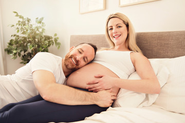 Beautiful pregnant woman and her handsome husband spending time together in bed