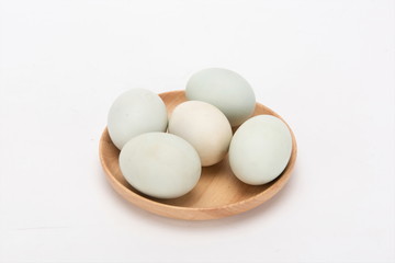 A few duck eggs are placed on a wooden plate, isolated against a white background