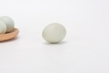 A few duck eggs are placed on a wooden plate, isolated against a white background