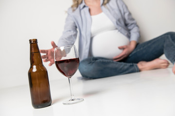Pregnant women drinking beer on studio white