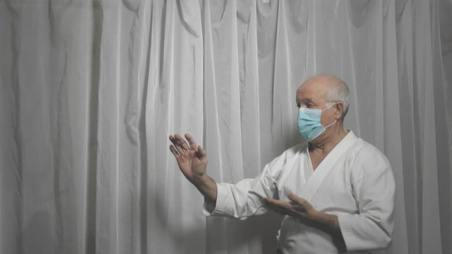 Adult athlete in medical mask trains karate formal exercises