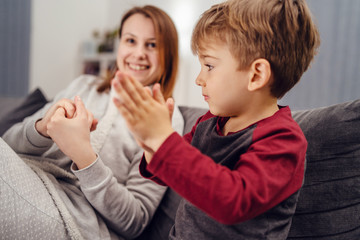 Portrait of small caucasian boy male child kid sitting on the sofa bed at home by mother young woman rubbing hands with alcohol disinfectant antibacterial prevention hygiene product prevent disease