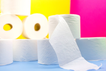 Many toilet paper rolls with one unrolled in front at home of hoarder on yellow blue pink color background hoarding amid panic buying for corona virus outbreak shortage.