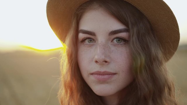 Close portrait of lady in a hat looking into camera with light smile wheat field