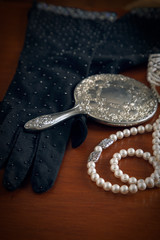 Vintage silver mirror, beaded gloves, pearls, compact and bracelets on a wooden dresser