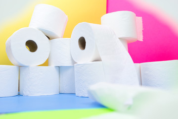 Pile of toilet paper rolls and one roll in front with camera wrapping effect on yellow blue pink color background hoarding amid panic buying for corona virus outbreak shortage.