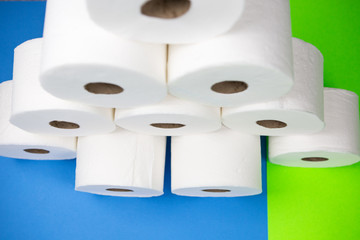 Ten toilet paper rolls in shape of a pyramid shown on light blue and bright green background. fear of corona virus outbreak closing shopping stores.