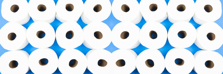 Background pattern mosaic of toilet paper rolls lay flat on the bright blue background. Coronavirus pandemic panic shopping concept. Banner size