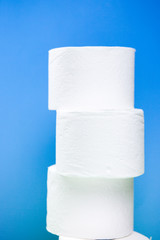 three white toilet paper rolls build a pyramid shown on light blue background.
