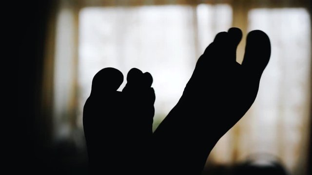 The man moves his feet flexing them. Visuet feet on the background of the window