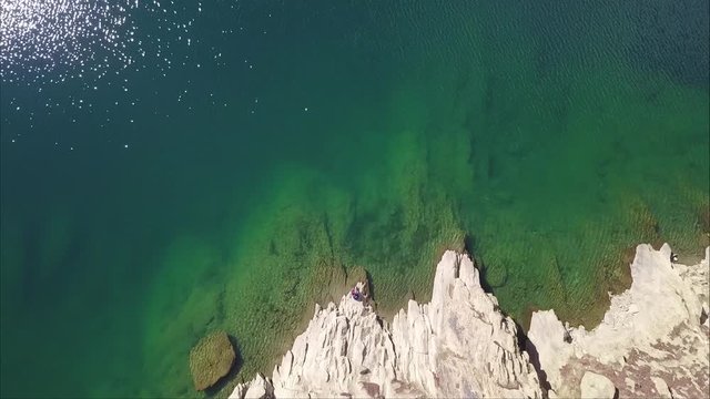 Aerial view of lulusar lake in pakistan zooming out towards top showing lush green color of water and a traveler sitting at the bank