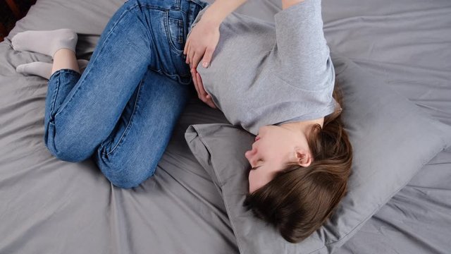 Unhappy young woman lying in bed holding belly suffering from stomach pain feeling painful discomfort hurt abdomen ache having pancreatitis problem, indigestion symptom. Stomachache concept