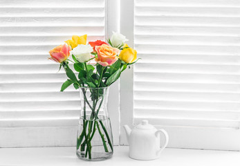 Bouquet with multicolored roses on a window with wooden blinds on a light background