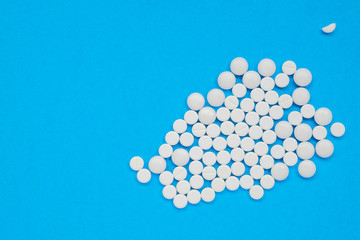 Lots of white pills on a blue background. Search for a cure for COVID-19, medicine concept. Horizontal orientation. Selective focus. Copy space. View from above.