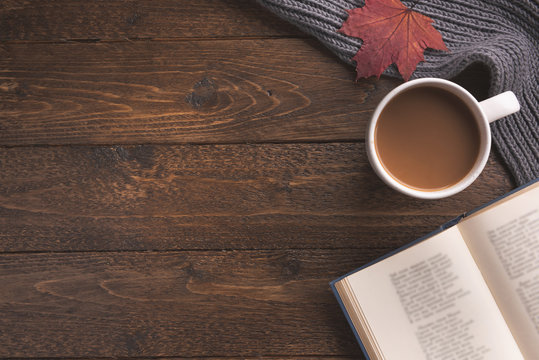 Flatlay composition with knitted scarf, cup of coffe, book, and yellow leaves on wooden desk table. Hygge style, cozy autumn or winter holiday concept. Flat lay, top view, overhead.