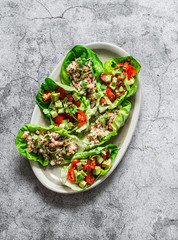 Leaves of mini roman salad stuffed with tuna, egg, tomato, avocado on a gray background, top view....