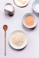 Ingredients for oat porridge: rolled oats or flakes, sugar, salt, milk and butter in a bowls on grey concrete background. Healthy eating, vegetarian food concept. Top view. Selective focus