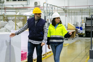 Two professional technicians walking at printing factory. Confident employees talking while walking...