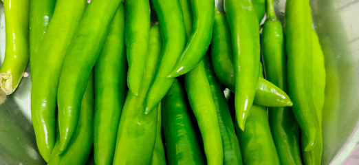 Full frame close up of a bunch of bright and shiny green chili peppers. Organic vegetables at the local food market.