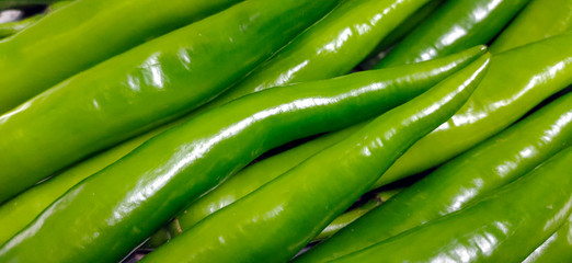 Full frame close up of a bunch of bright and shiny green chili peppers. Organic vegetables at the local food market.