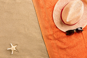 Top view straw hat and sunglasses with copy space. Traveler accessories on sand. Travel vacation concept. Summer background. Border composition made of towel