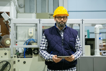 Front view of technician holding tablet at plant. Confident factory worker using tablet while...