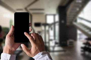 Hand held black phone With a blank white screen in the Gym in the morning light.