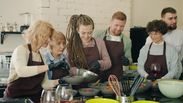 Happy people in aprons are cooking meals enjoying cookery master-class indoors working with professional chef. Nutrition, leisure time activitites and apprenticeship concept.