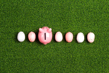 Piggy bank with pink eggs on a green grass background.